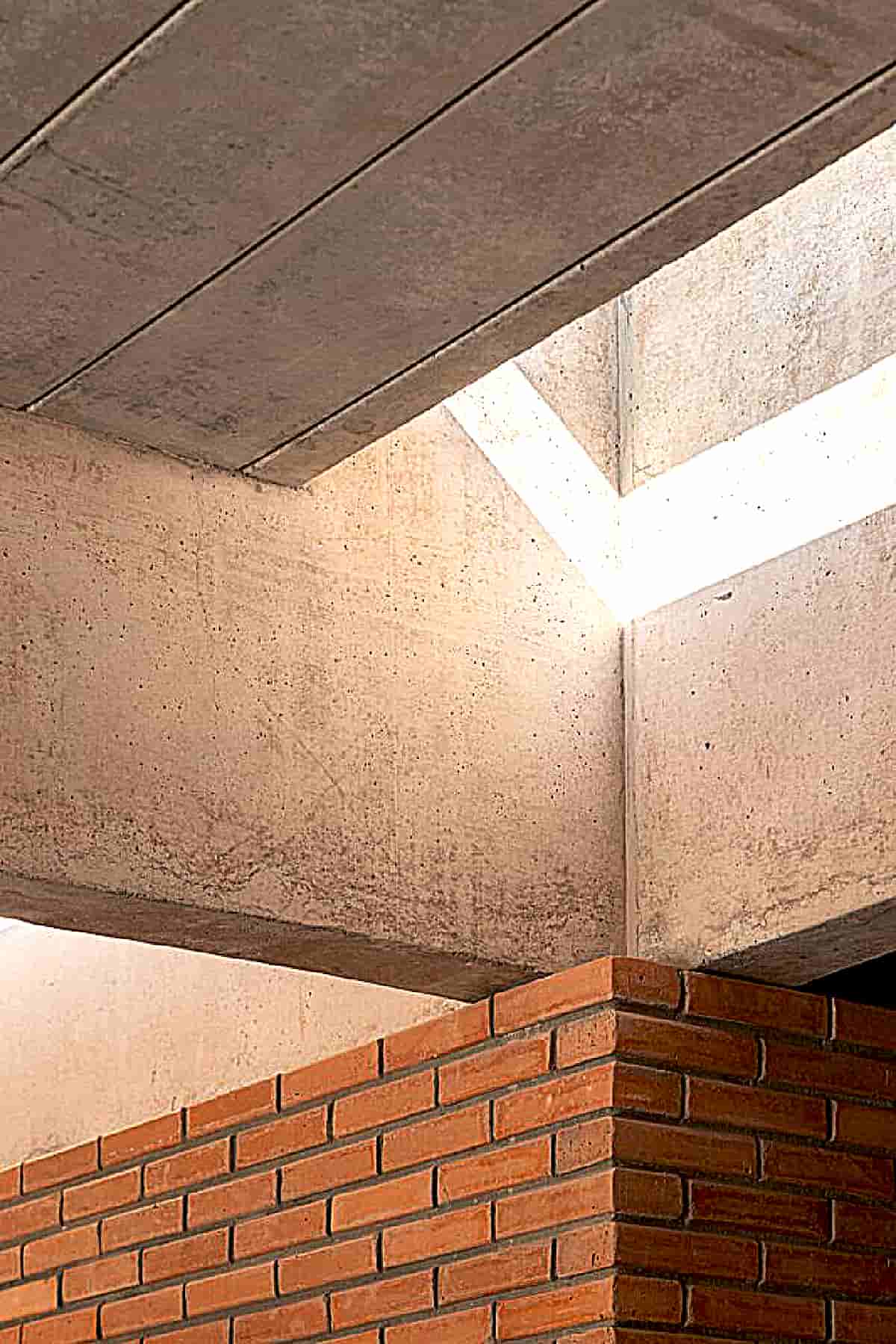 2-1txt) [The roof structure of the house is formed by 8 exposed concrete beams cast in place. With a length of 30.5 meters and spaced 2.10 meters apart. The beams are interspersed with exposed beams of the slab-panel type. A second mesh of perpendicular beams follows the internal divisions of the rooms and “ties together” the whole structure]. At some specific points (access gallery, bathrooms, circulations and internal sections of the room and balcony); The placement of the slab-panel joists is interrupted by linear skylights for natural lighting and/or ventilation. Most of the luminaires are built into these skylights.
