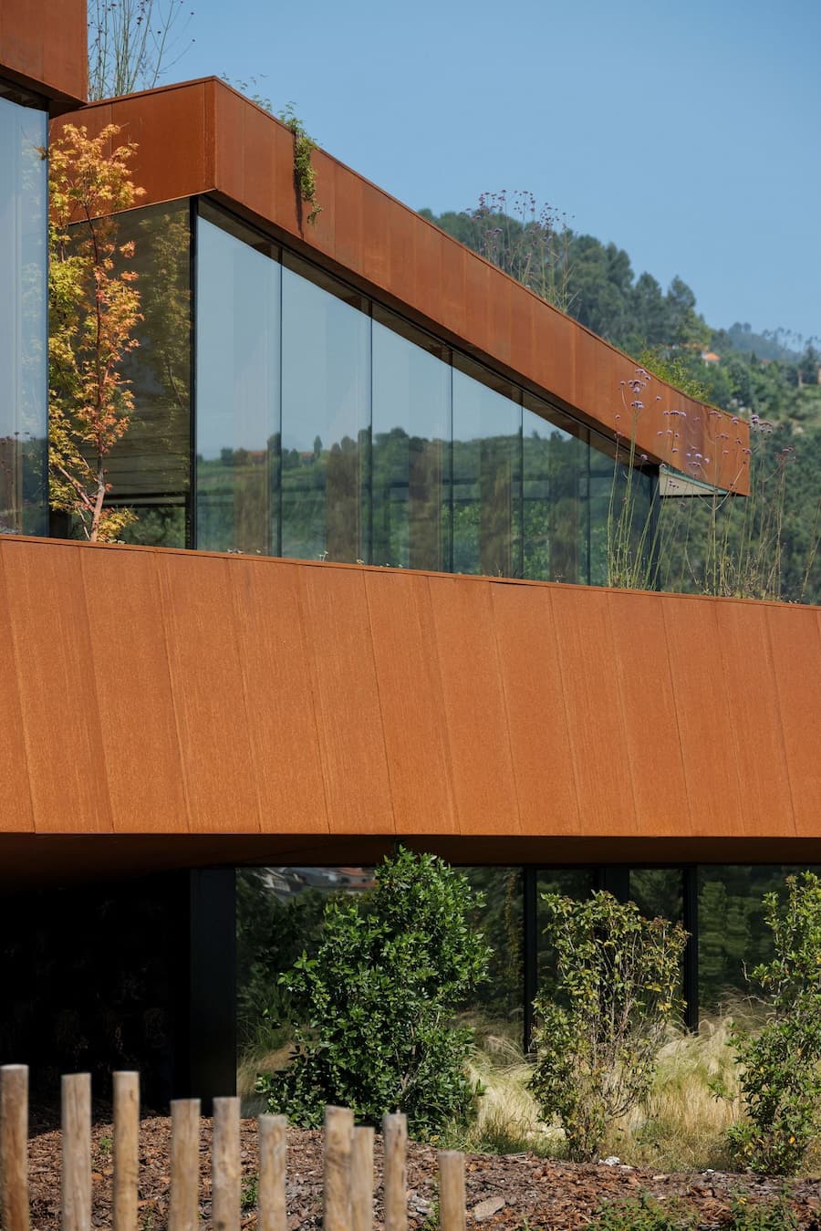 glass facade framed by weathering steel reflecting surrounding vegetation