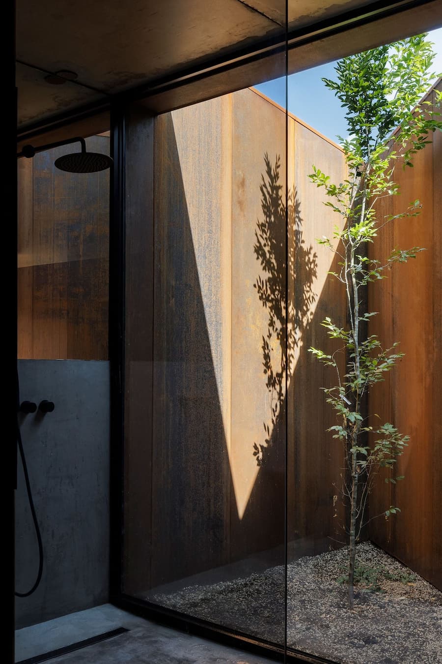 outdoor shower facing small courtyard with corten steel wall and filtered daylight