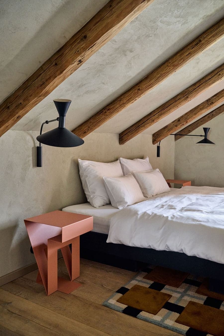 bed positioned under sloped roof with exposed timber beams