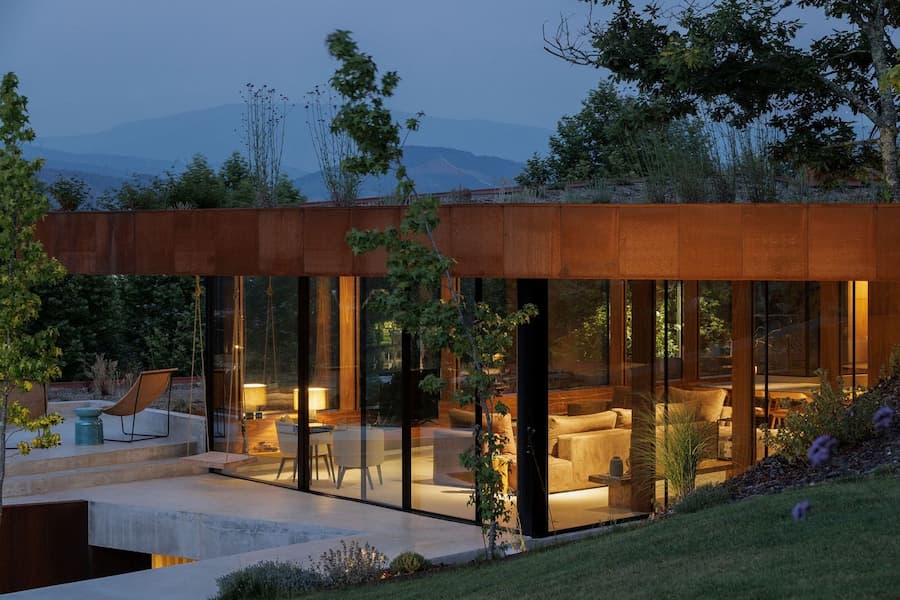 glass facade revealing interior lighting system within corten volume at dusk