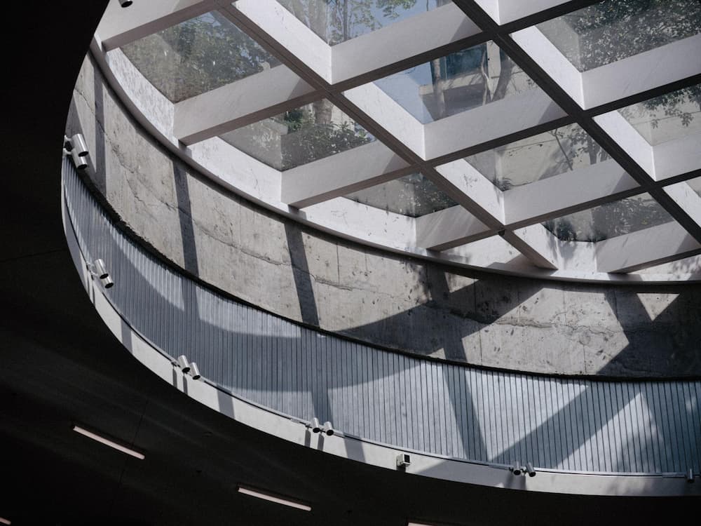natural light entering a concrete interior through a skylight grid, casting geometric shadows across curved surfaces