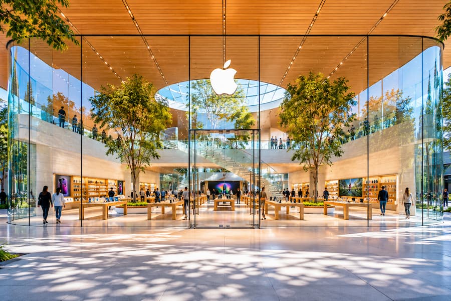 Contemporary Apple Store architecture featuring curved glass walls, natural light, timber ceiling, indoor trees, and minimalist spatial design reflecting Apple’s architectural language