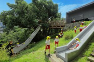 children playing on grassy hillside slides integrated with architecture and natural landscape to reimagine childhood play experiences