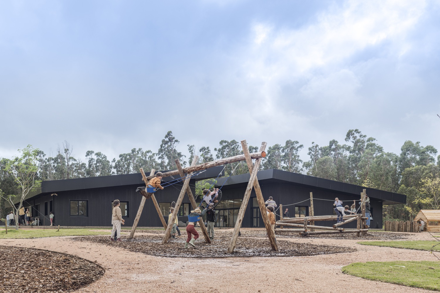 children playing in outdoor natural playground beside low horizontal learning campus