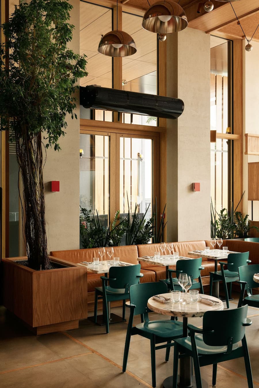 Contemporary restaurant interior with marble tables, leather banquette seating and indoor trees