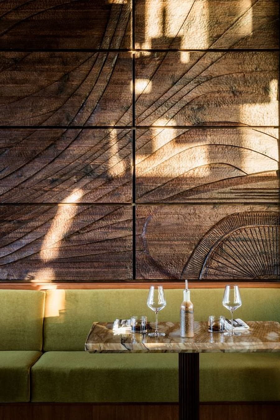 Restaurant interior with carved wood wall art, green banquette seating and marble tables