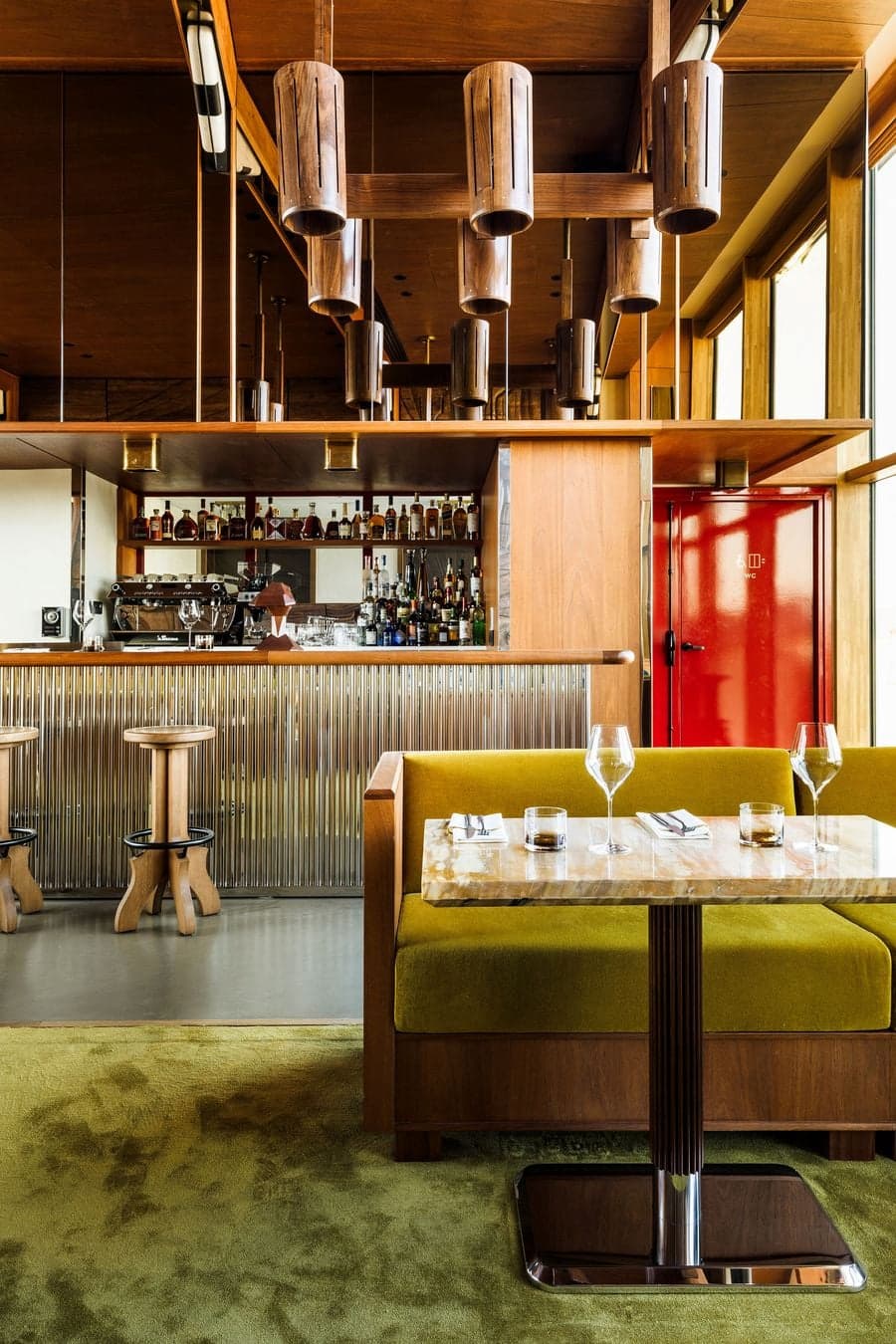 Boutique hospitality bar with green banquette seating, wood ceiling and metallic finishes
