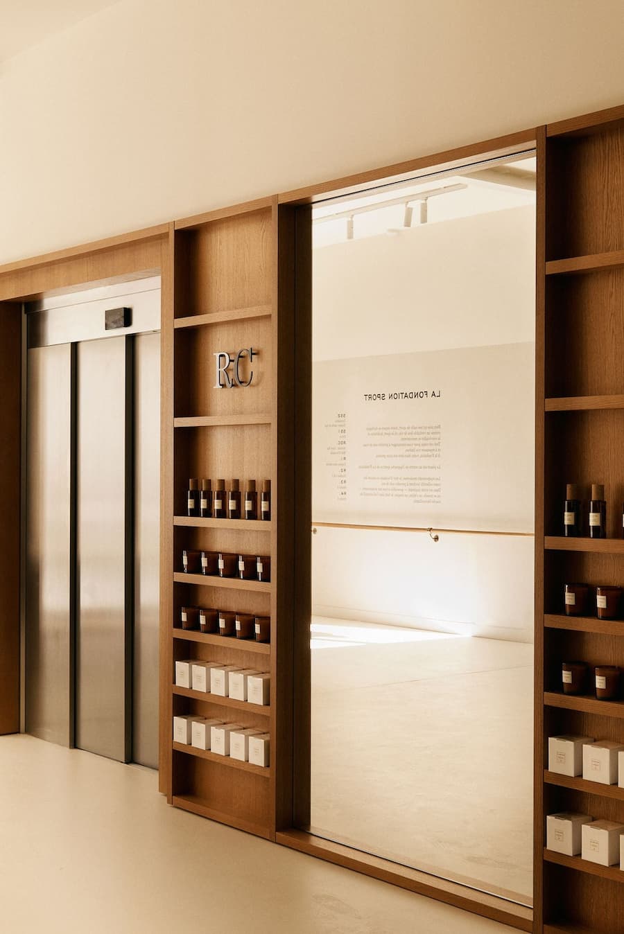 Oak retail shelving and mirrored passage within a refined minimalist store interior