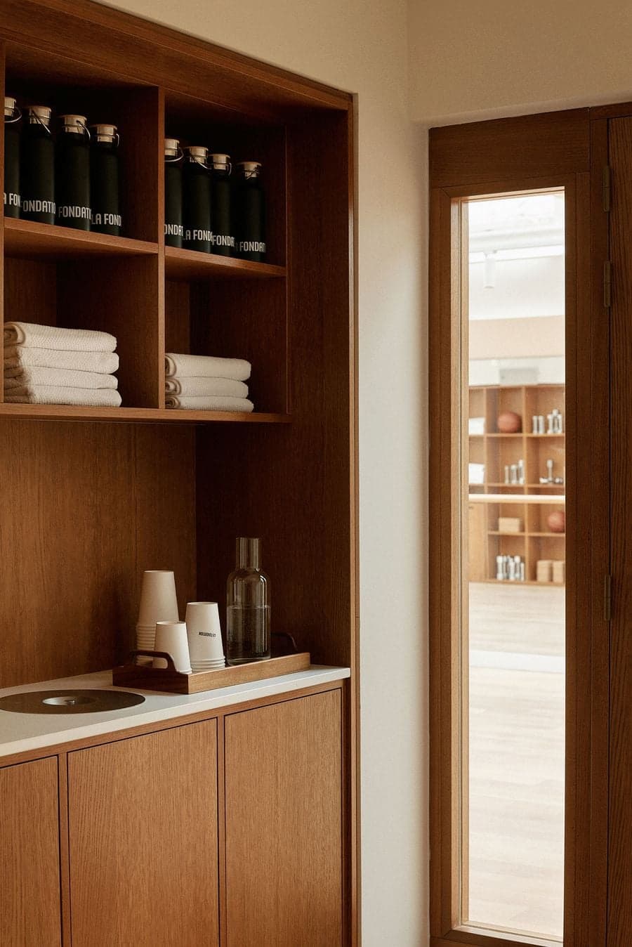 Wellness refreshment station with warm wood cabinetry, towels and minimalist detailing