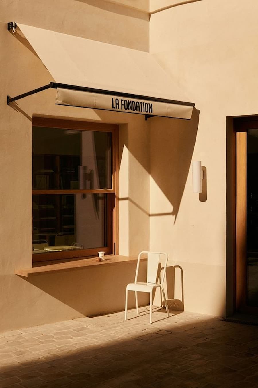 Minimal courtyard architecture with branded awning, soft shadows and warm neutral palette