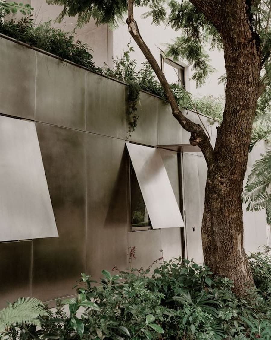 Reflective metal facade of Barrancas House by PPAA blending with surrounding trees in Mexico City