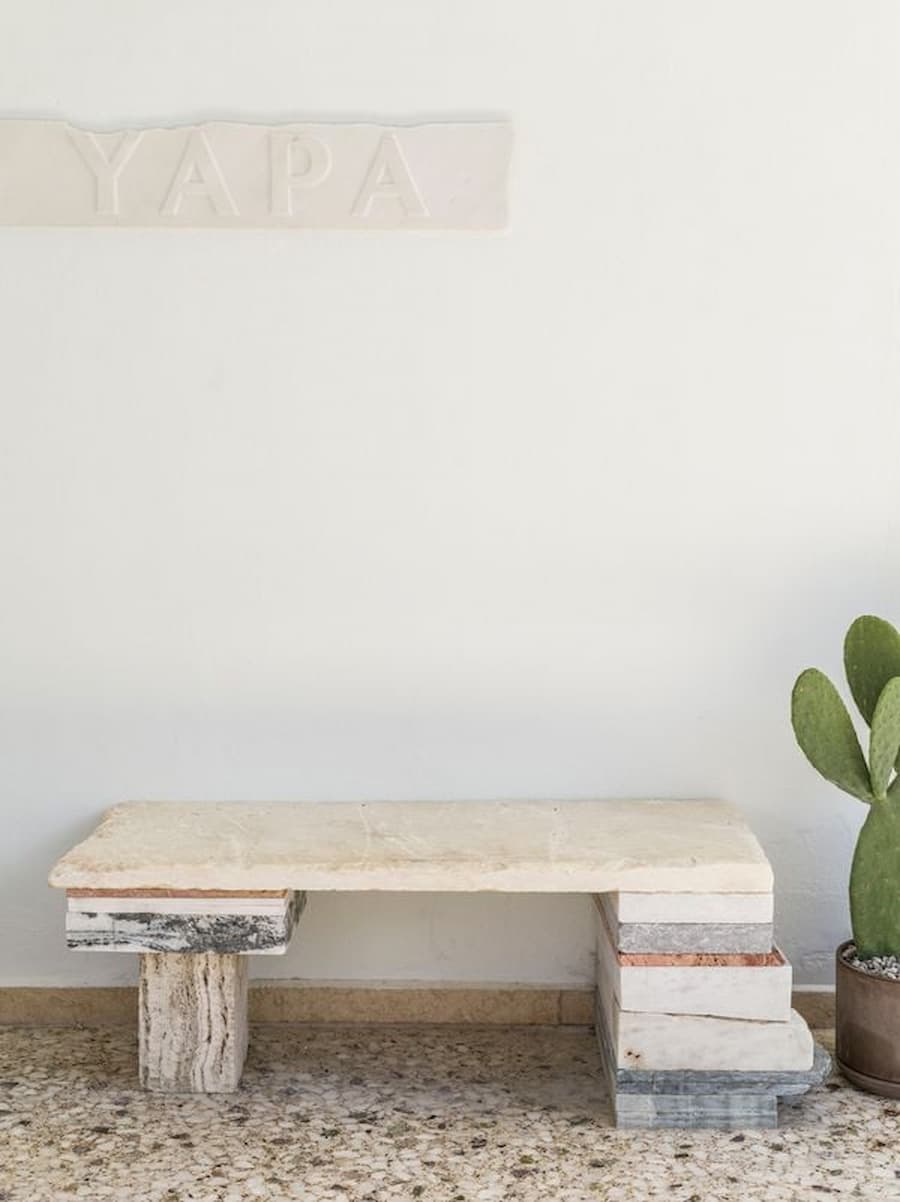 Stone bench crafted from layered reclaimed marble beneath the YAPA sign inside the restored Cycladic restaurant in Antiparos, Greece