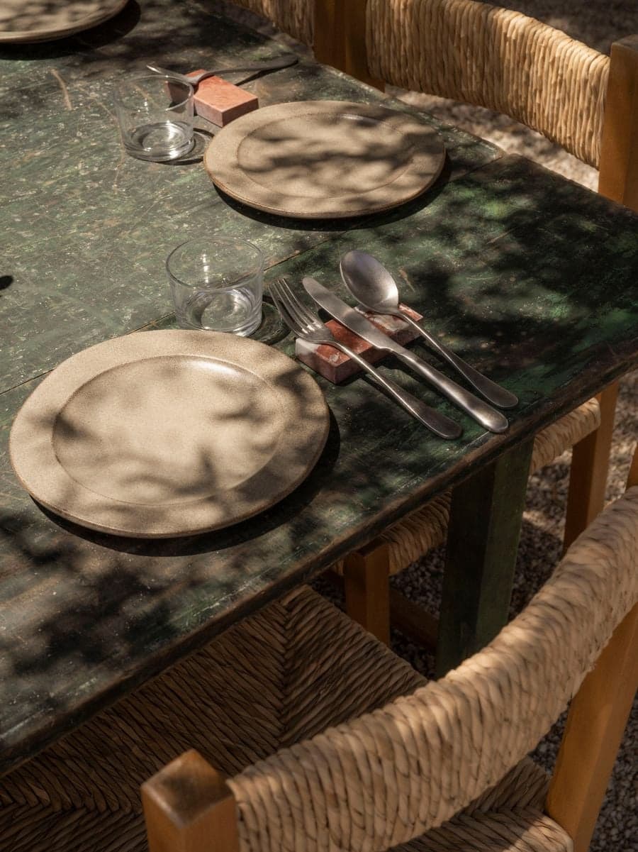Communal marble dining table with handcrafted tableware and woven timber chairs at YAPA Antiparos outdoor dining courtyard