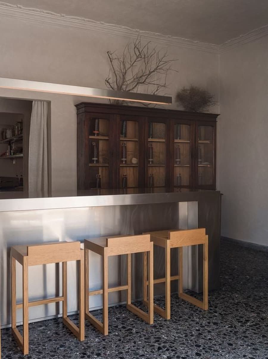 Minimal stainless steel bar counter with solid oak stools inside YAPA Antiparos, blending Cycladic architecture with contemporary restaurant design