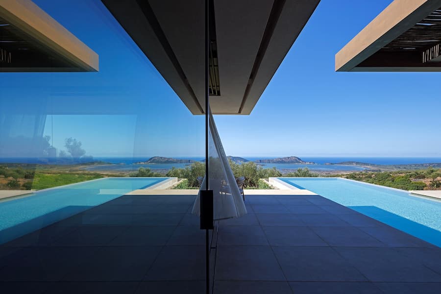 Reflection across full-height glazing framing the infinity pool and Navarino Bay
