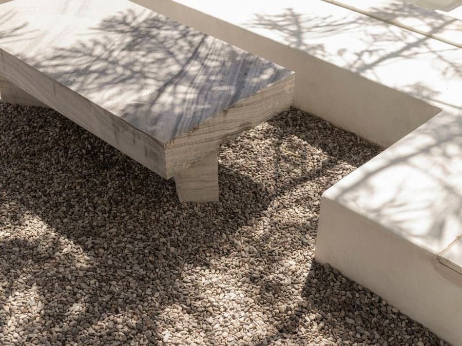 Handcrafted marble bench surrounded by natural gravel and soft tree shadows at YAPA Antiparos restaurant courtyard