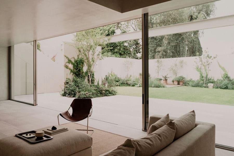 Living room framed by floor-to-ceiling glazing opening toward the landscaped garden