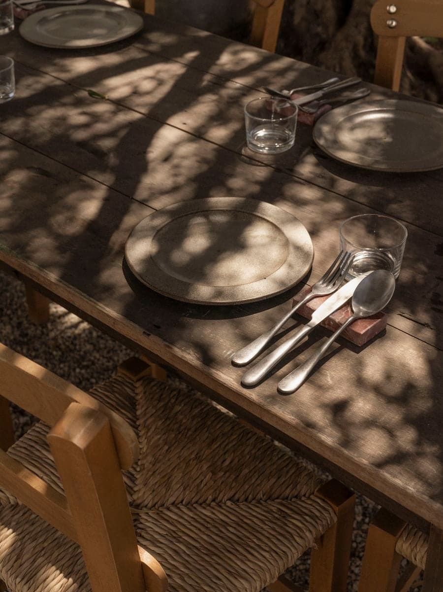 Natural table setting with handcrafted ceramics and woven chairs beneath olive tree shadows at YAPA Antiparos