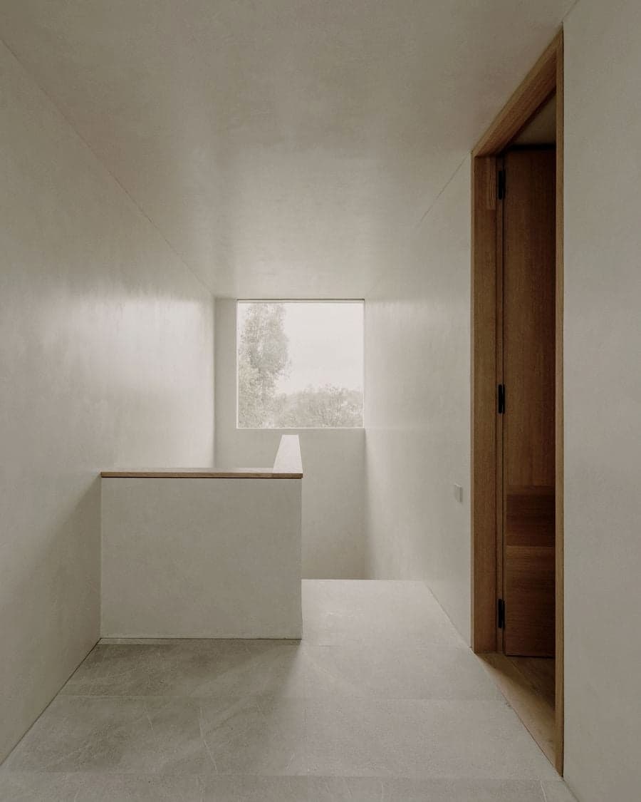 Upper hallway finished with pale plaster walls and a square window framing the trees