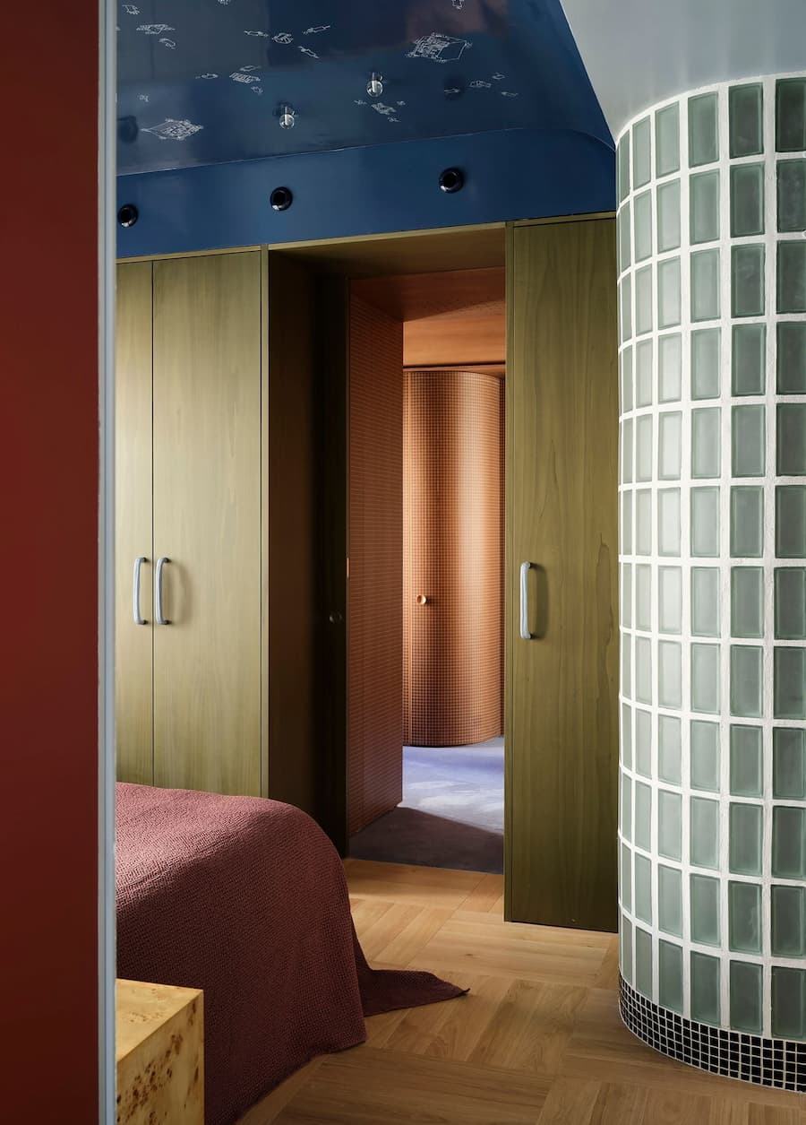 Bedroom framed by a curved glass block wall, blue ceiling and custom built-in cabinetry.