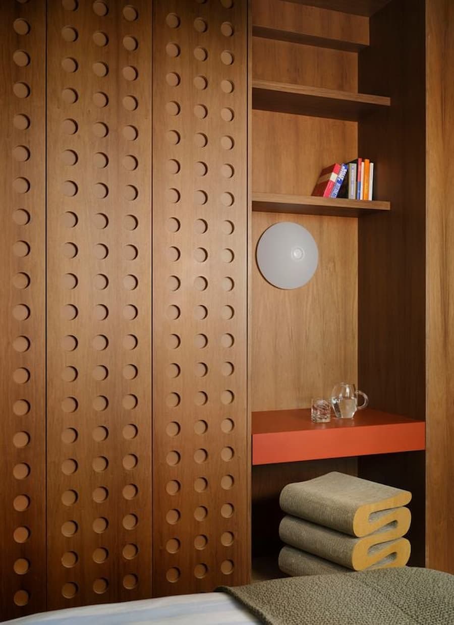 Custom perforated wood wardrobe integrates shelving, workspace and handcrafted storage details.