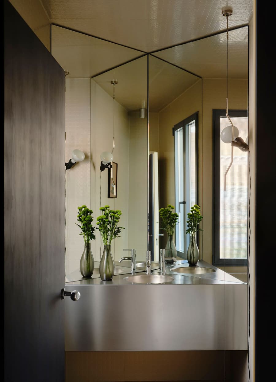 Stainless steel bathroom vanity with mirrored walls creates layered reflections and spatial depth.