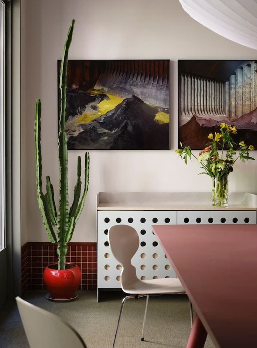 Dining corner featuring contemporary artwork, perforated storage cabinet and sculptural cactus display.
