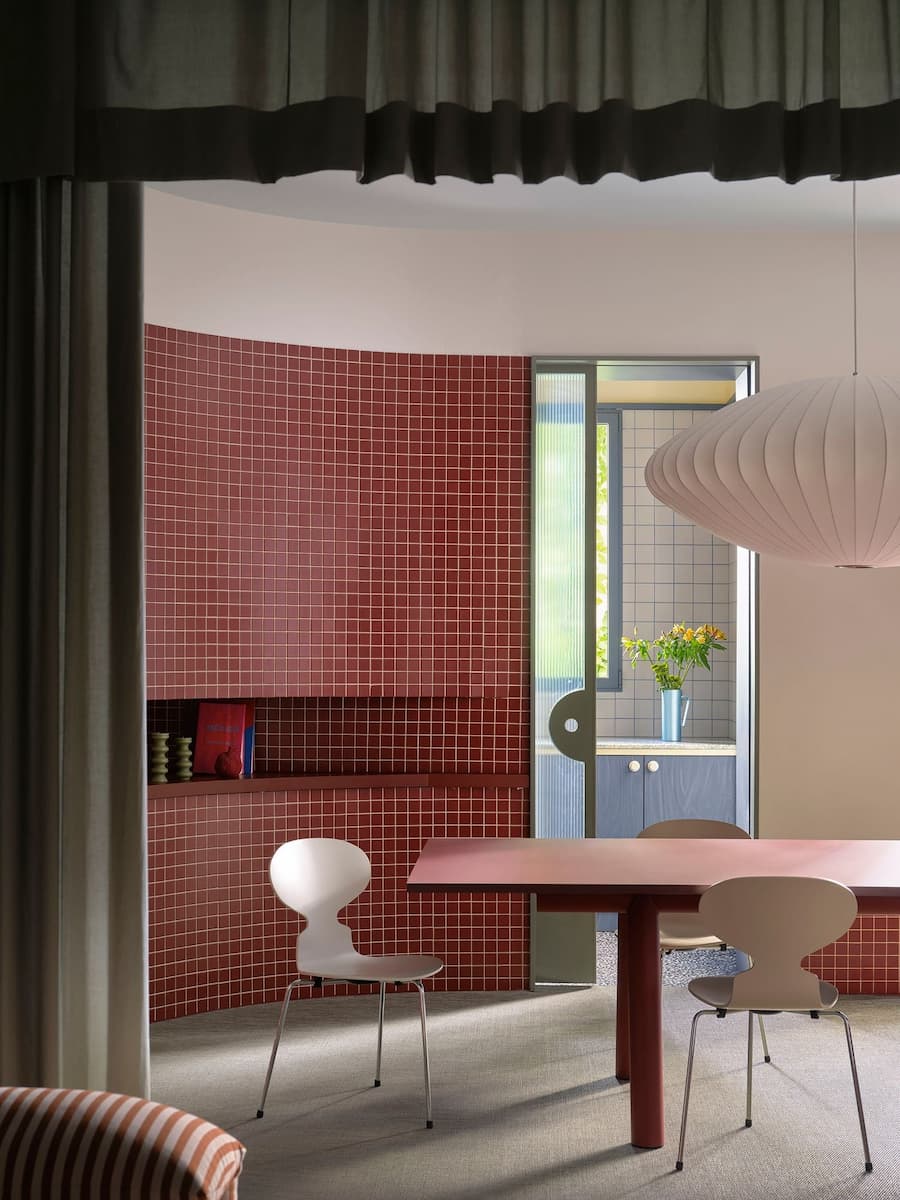 Dining room defined by curved red mosaic tiles, custom table and soft diffused daylight.