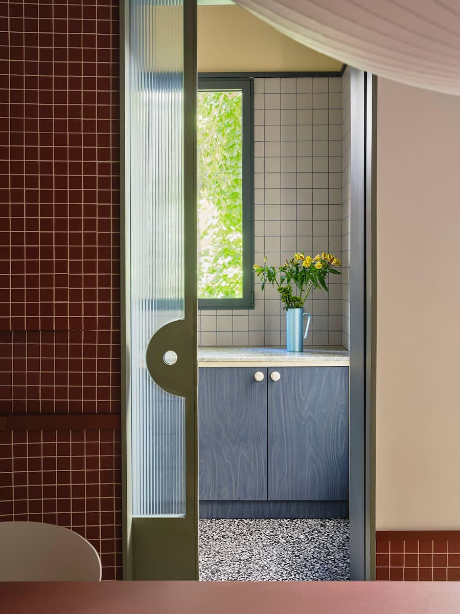 Fluted glass sliding door connects the dining area with the blue plywood kitchen.