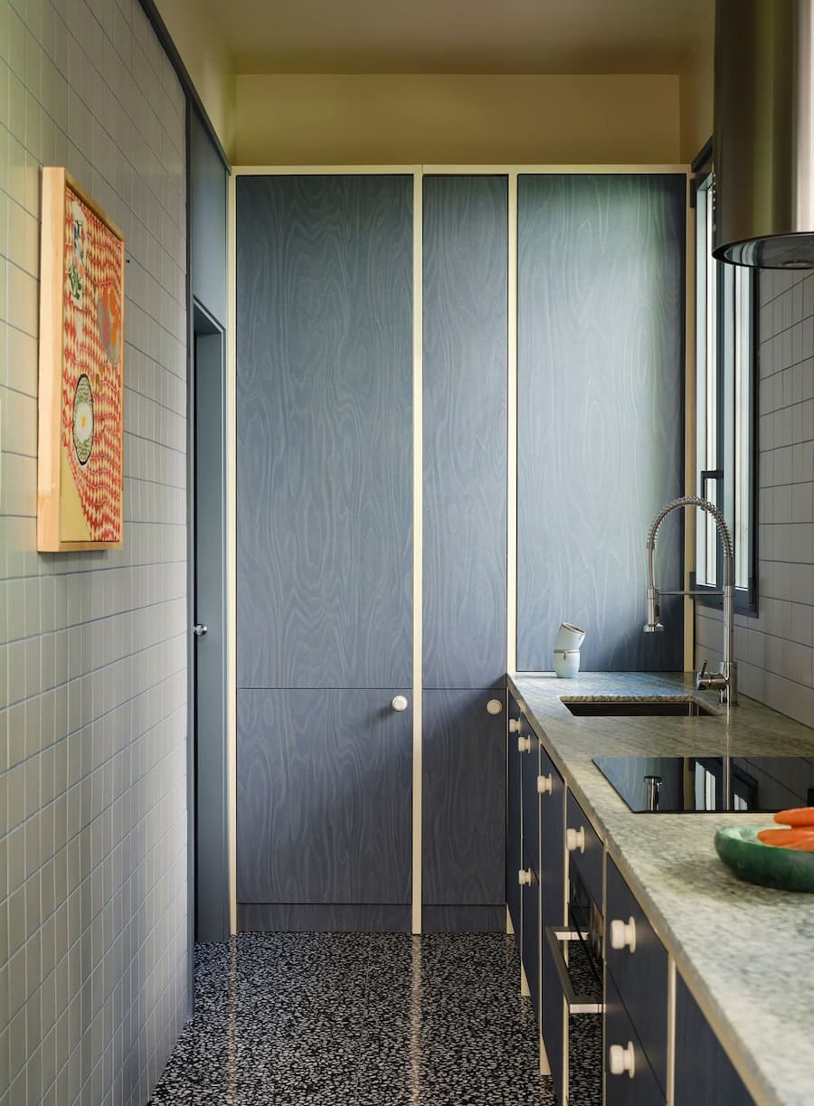 Custom blue plywood kitchen paired with terrazzo flooring, stone countertop and minimalist cabinetry.