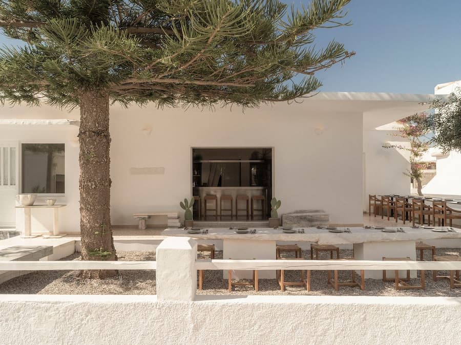 Courtyard dining framed by Cycladic architecture and Mediterranean pine trees at YAPA Antiparos, Greece