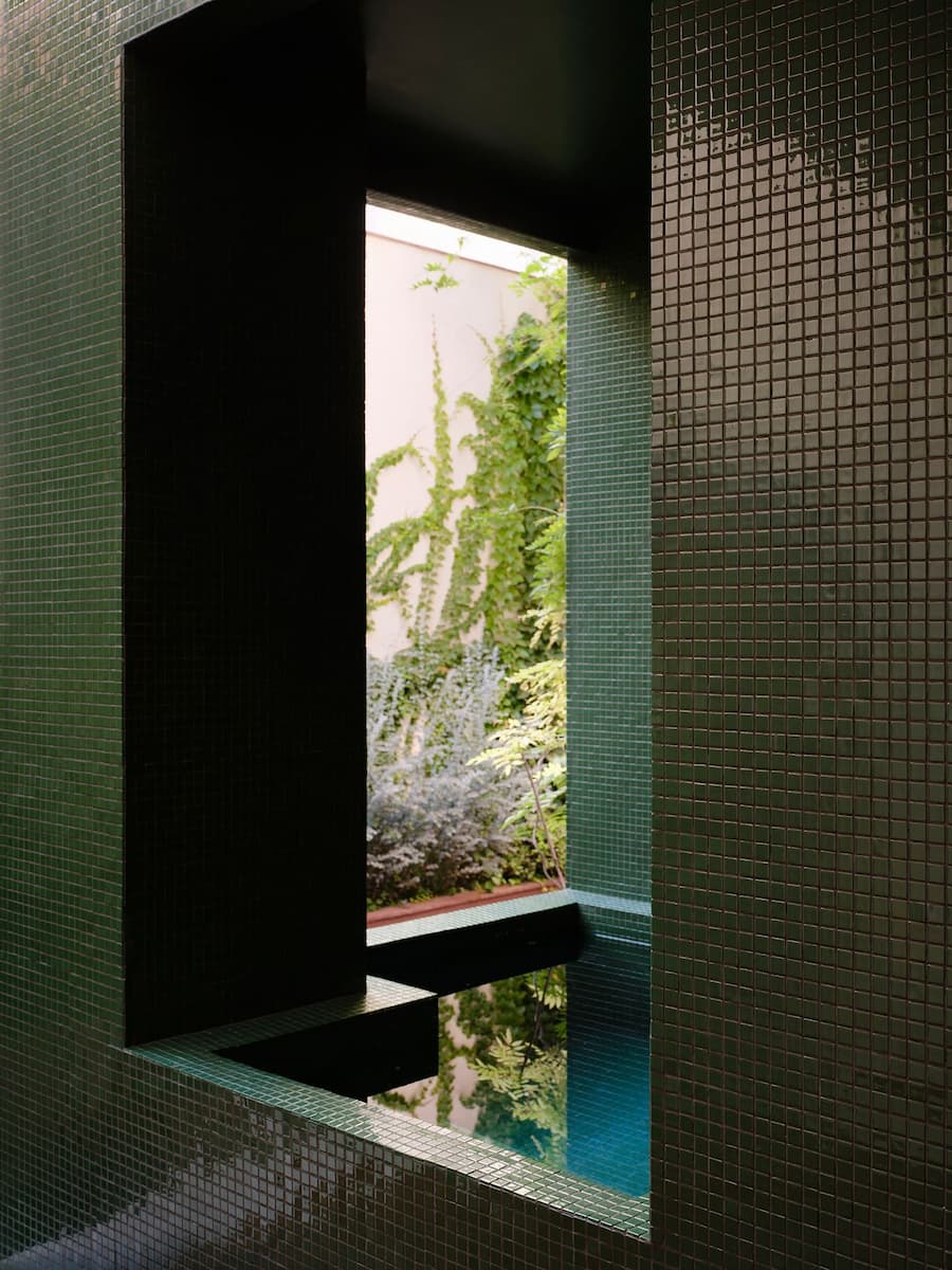 Green mosaic courtyard frames a tranquil water feature and lush planting with filtered natural light.