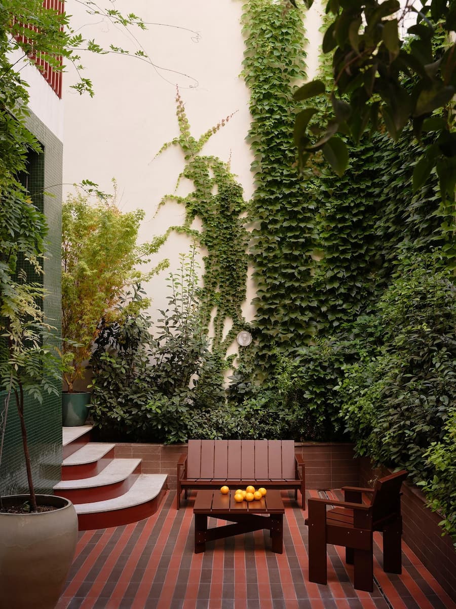 Lush courtyard lounge framed by climbing greenery, terracotta paving and custom outdoor seating.