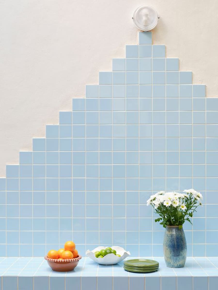 Outdoor kitchen finished with pale blue tiles, integrated counter and decorative still-life arrangement.