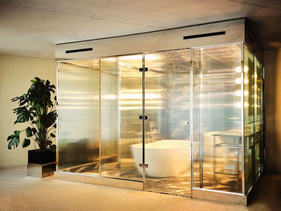 Freestanding bathtub enclosed by ribbed glass and warm ambient lighting