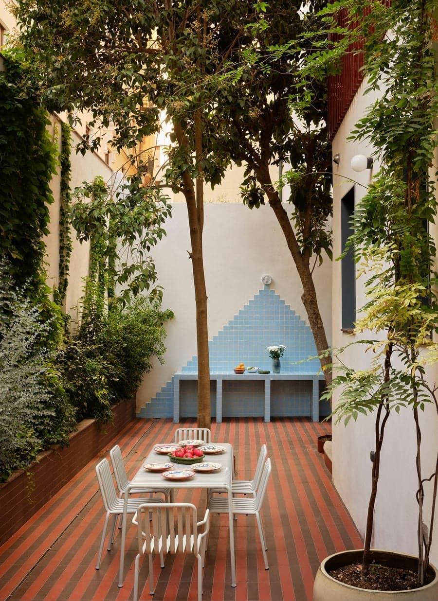 Courtyard dining area surrounded by mature trees, climbing plants and handcrafted blue tiled outdoor kitchen.