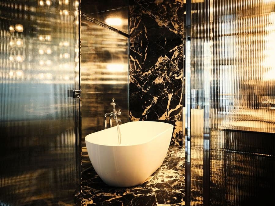 Black marble bathroom with freestanding bathtub framed by ribbed glass partitions