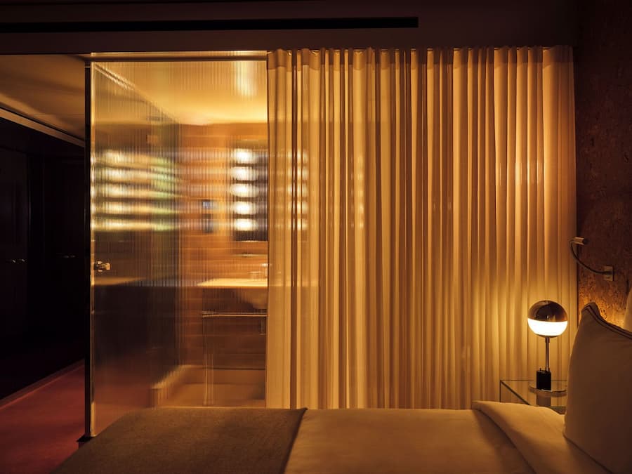 Soft evening light filters through ribbed glass and sheer curtains in the hotel bedroom