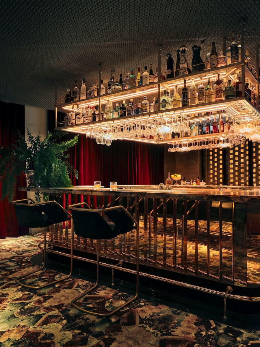 Backlit cocktail bar surrounded by velvet seating and vintage-inspired interiors
