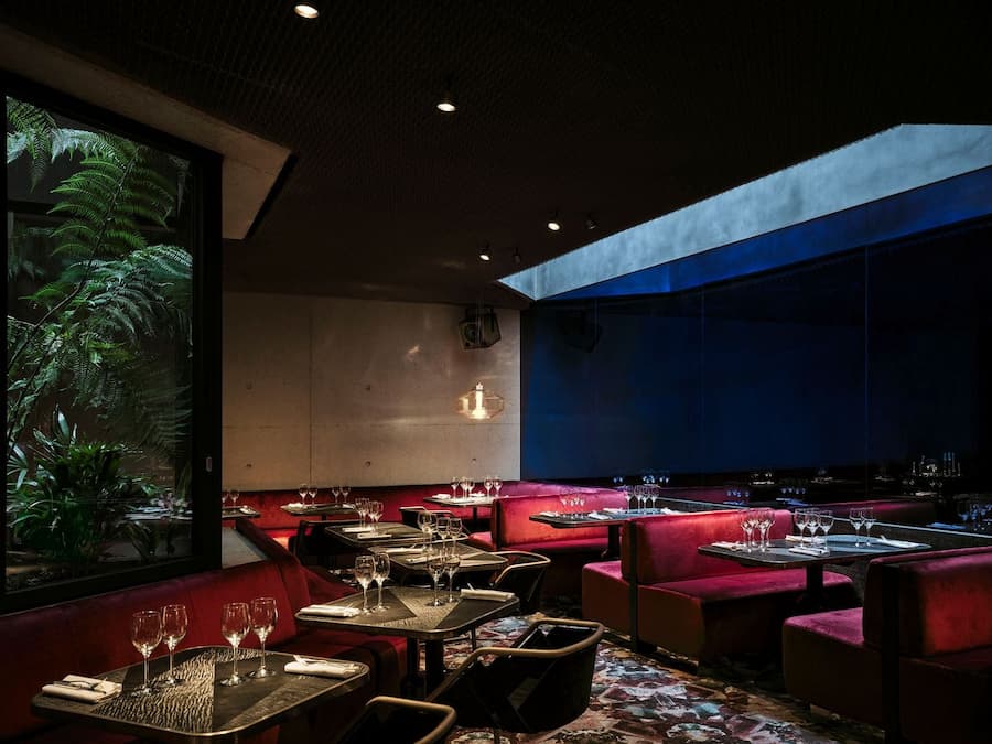 Deep burgundy banquettes create an intimate dining atmosphere beneath skylight illumination