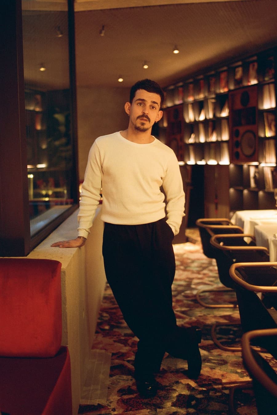 Restaurant chef standing inside the dining room framed by vinyl records and warm ambient lighting