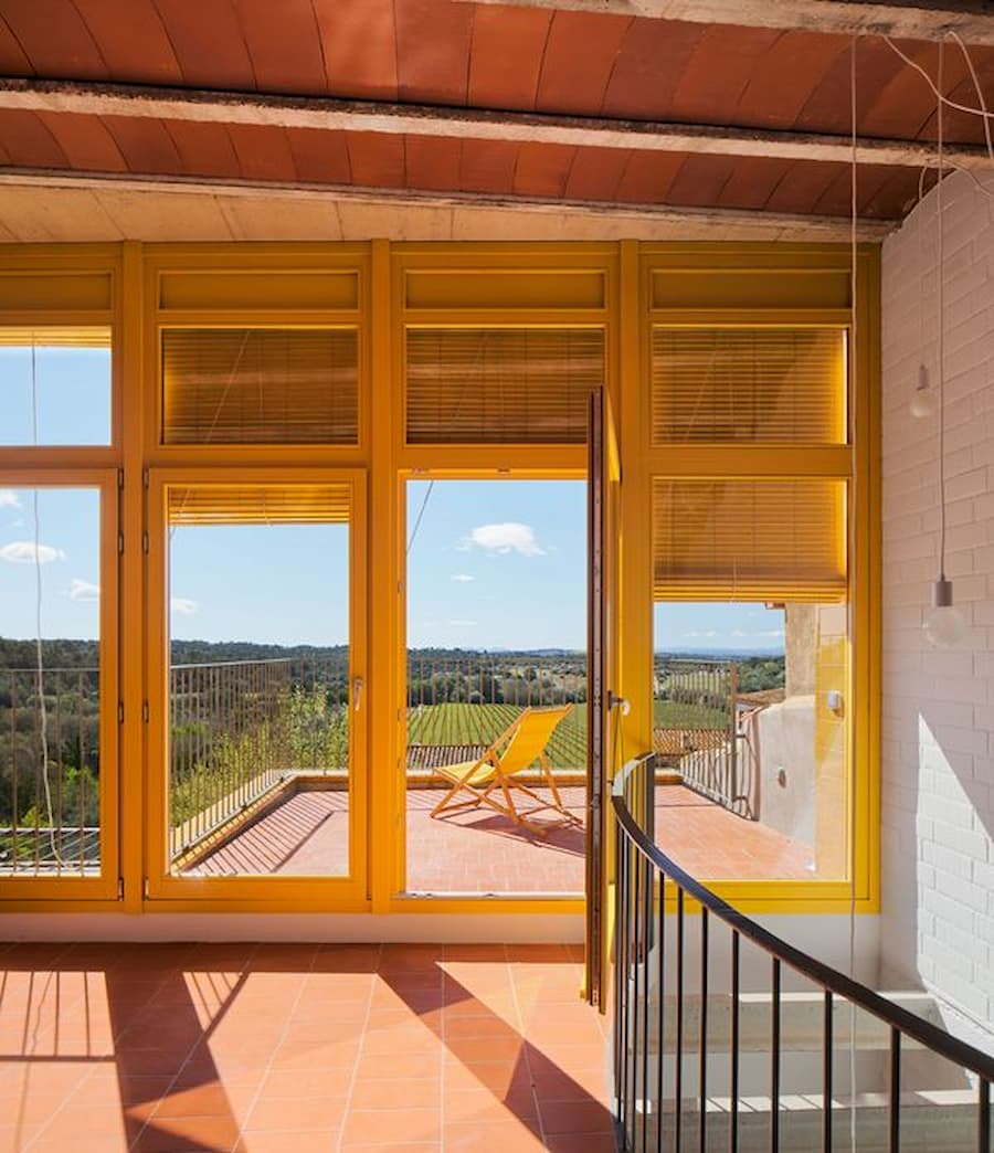 Open living space facing the terrace through bright yellow window frames at Ca la Carolina by Lacol and Altura Arquitectes.