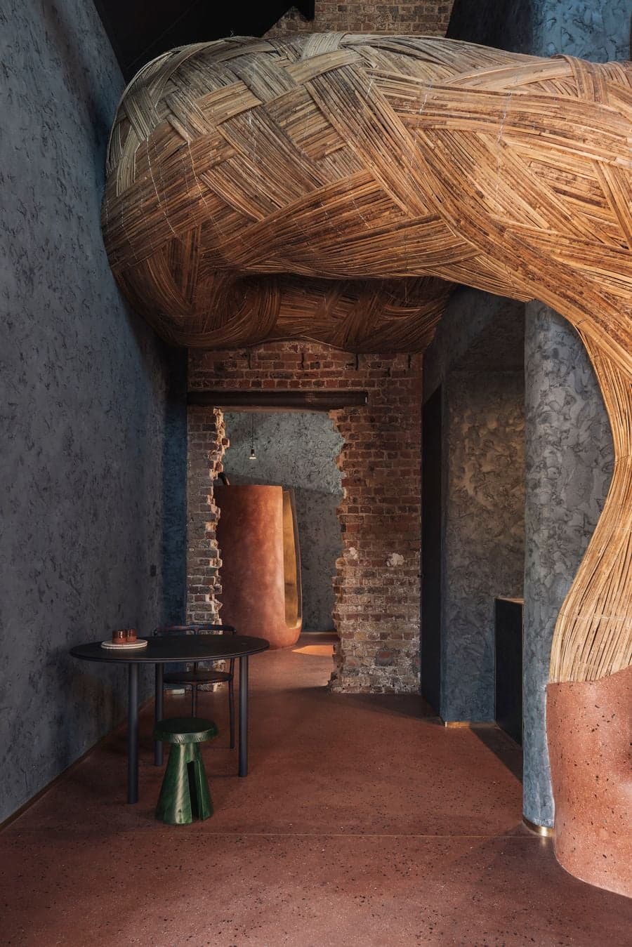 A sculptural woven bamboo ceiling curves through a corridor framed by exposed brick walls