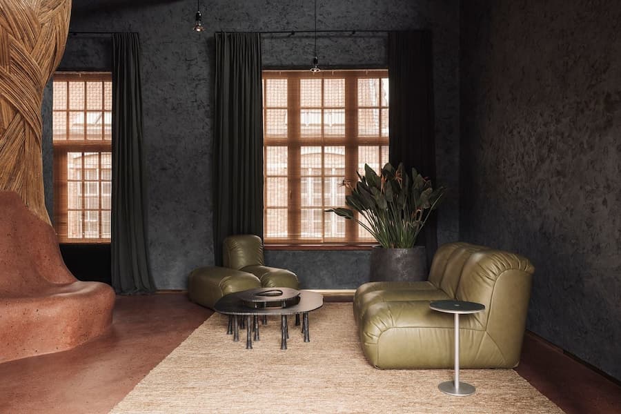 Olive leather lounge seating arranged beneath timber windows with woven bamboo blinds