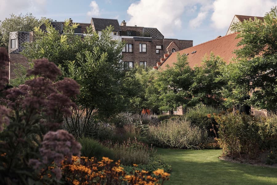A lush garden courtyard surrounded by historic brick buildings and terracotta rooflines in Bruges