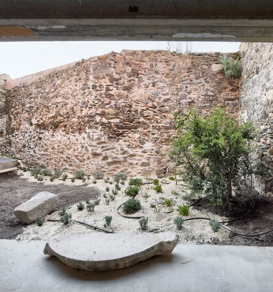 Stone courtyard garden beneath Ca la Carolina preserving the original village walls.