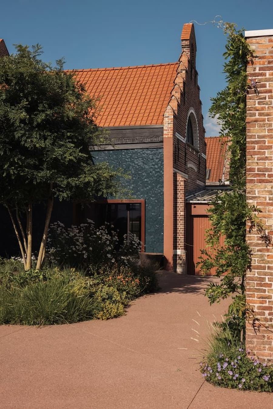 A terracotta-toned pathway leading through native planting beside an old brick building