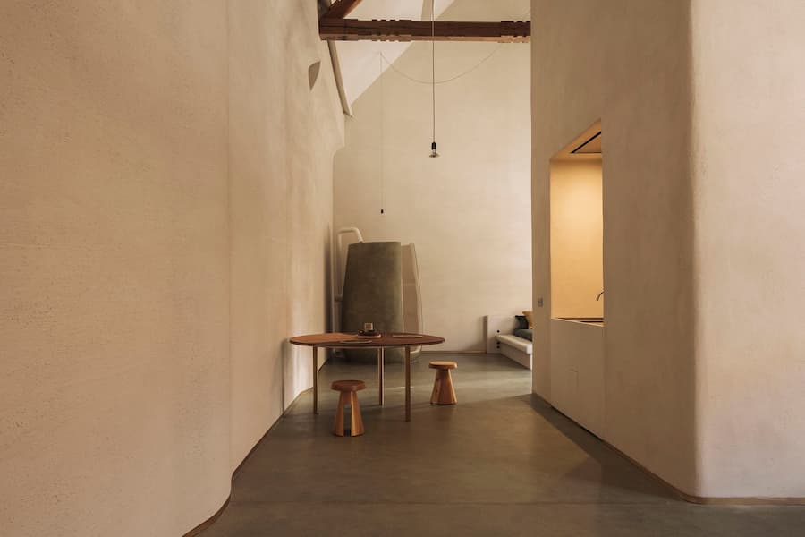 An earth-toned suite featuring a sculptural freestanding bath, wooden stools and a round dining table