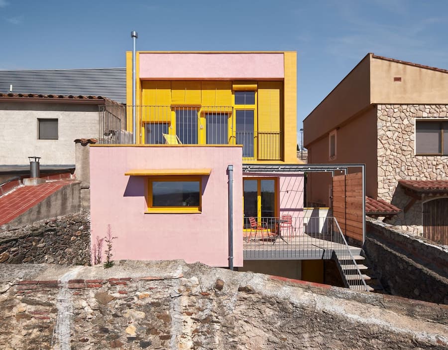Front elevation with terrace and yellow facade at Ca la Carolina by Lacol and Altura Arquitectes.